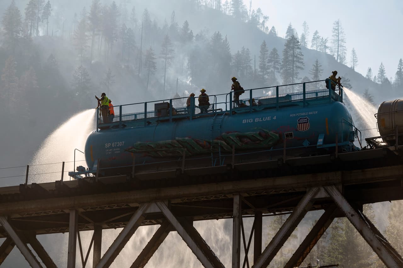 Los bomberos rocían agua desde el tren de bomberos de Union Pacific Railroad mientras luchan 
<i><a href="https://www.univision.com/noticias/estados-unidos/oregon-california-enorme-incendio-oeste-de-estados-unidos" target="_blank">contra el incendio Dixie</a></i> en el Bosque Nacional Plumas, California.