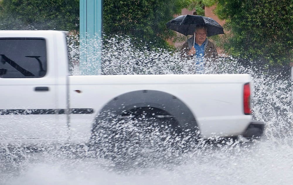Un hombre espera un autobús en Anaheim mientras un carro levanta el agua acumulada por las tormentas.