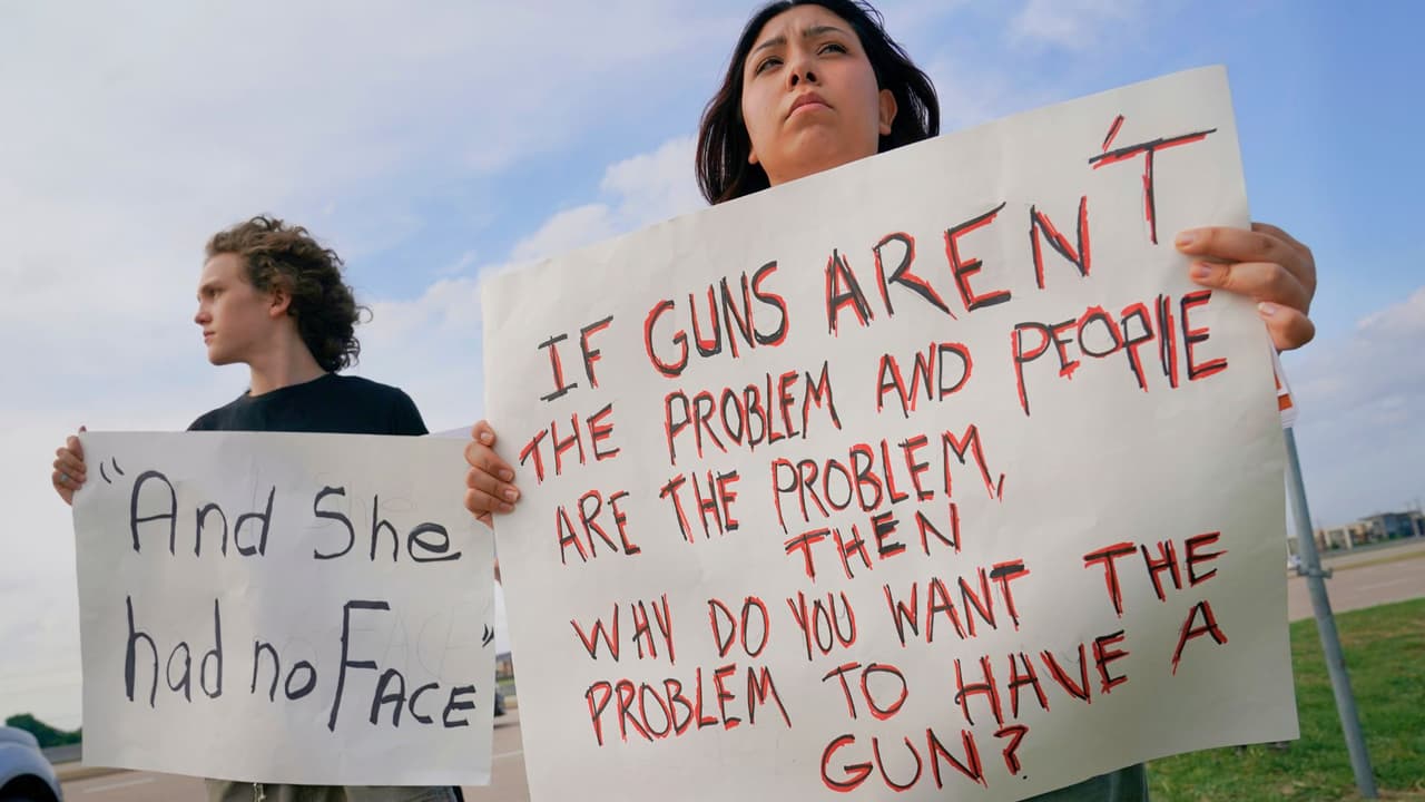 Sam Morin, de 17 años, a la derecha, y Briason Foley, de 15, sostienen carteles de protesta fuera de una vigilia de oración después de un tiroteo masivo en la víspera del domingo 7 de mayo de 2023, en Allen, Texas.