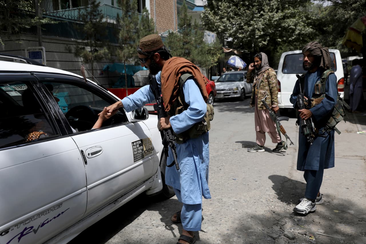 En Kabul, grupos de combatientes con fusiles han patrullado los vecindarios donde se encuentran muchas embajadas, así como mansiones de la elite afgana. En la fotografía un militante talibán saluda a los que pasan por un punto de control en Kabul, el 18 de agosto.
<br>