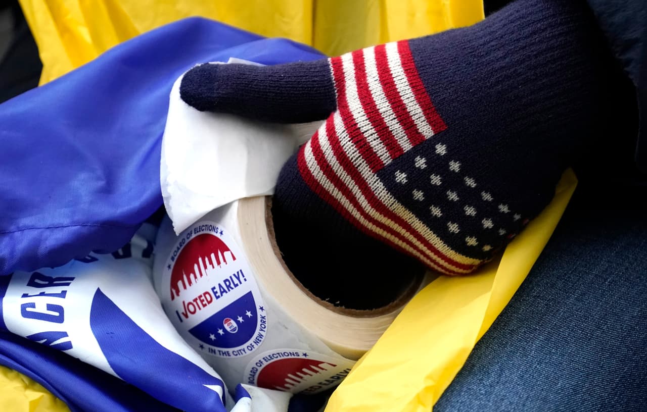 Un trabajador electoral distribuye calcomanías, el viernes antes de las selecciones, mientras los primeros votantes se envuelven en la cuadra esperando votar en la escuela secundaria Robert Wagner en el Upper East Side de la ciudad de Nueva York. Según reportes, la escuela es el centro de votación más concurrido de la ciudad donde los votantes, en algunos casos, esperan hasta seis horas para emitir su voto.