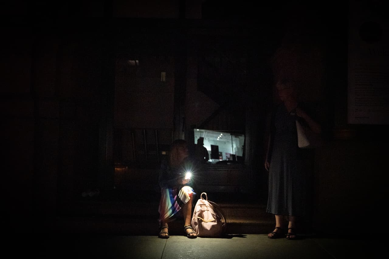 NUEVA YORK, NY - 13 DE JULIO: Una mujer se sienta en los escalones del Carnegie Hall usando su teléfono celular como linterna durante el apagón. (Foto de David Dee Delgado/Getty Images)