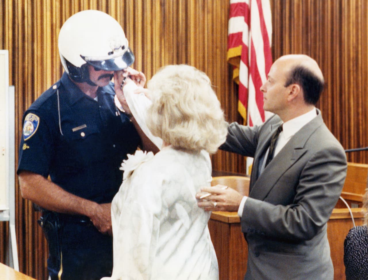 En una foto de archivo del 14 de septiembre de 1989, el abogado defensor William Graysen, a la derecha, coloca la mano de Zsa Zsa Gabor en el rostro del oficial de policía de Beverly Hills, Paul Kramer, durante una recreación del incidente del 14 de junio que resultó en el arresto de Miss Gabor.