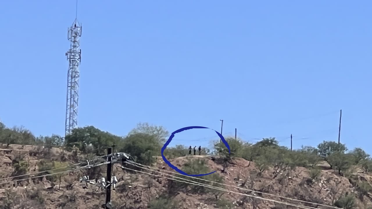 Arriba de la loma, al lado de la antena, se observan tres hombres, se les llama 'halcones' o 'puntos', así son reconocidos por las autoridades fronterizas. Ellos a través de binoculares alertan a los migrantes del momento en el que no hay agentes migratorios para que escalen el muro fronterizo.