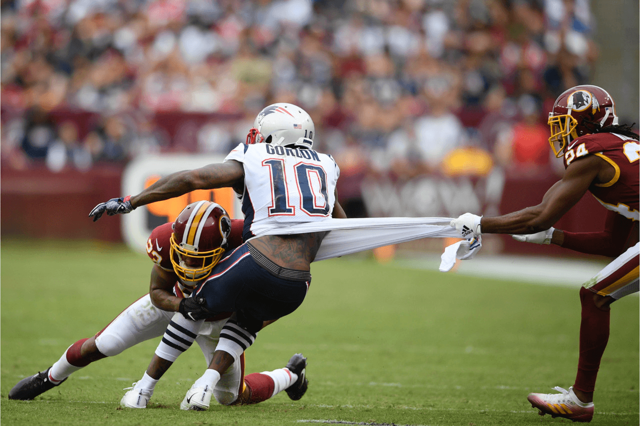 Dos jugadores de los Washington Redskins teclean al receptor Josh Gordon de los New England Patriots.