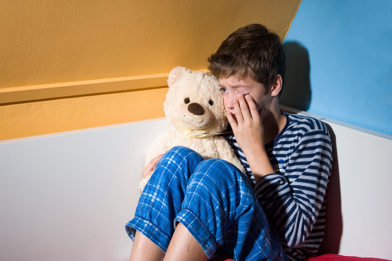 A young boy is crying on his bed in his bedroom