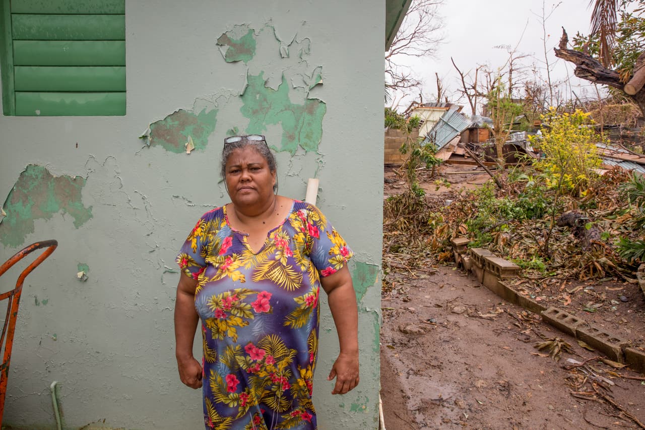 Yolanda Carmona es hermana y vecina de Alfredo. Con la casa derrumbada de fondo, cuenta que su hermano decidió salir de la casa unos instantes antes que el huracán la destruyera completamente. Asegura que por su residencia al norte de Vieques no ha pasado ninguna agencia local, nacional o federal ofreciendo ayuda.