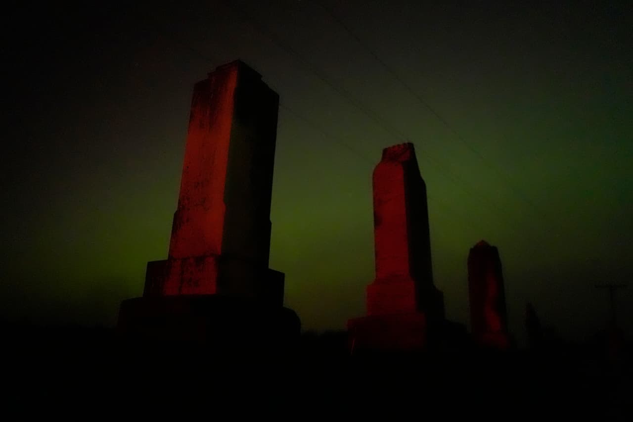 Lápidas antiguas se alzan con la aurora boreal de fondo en un cementerio la madrugada del sábado, cerca de Skidmore, Missouri.