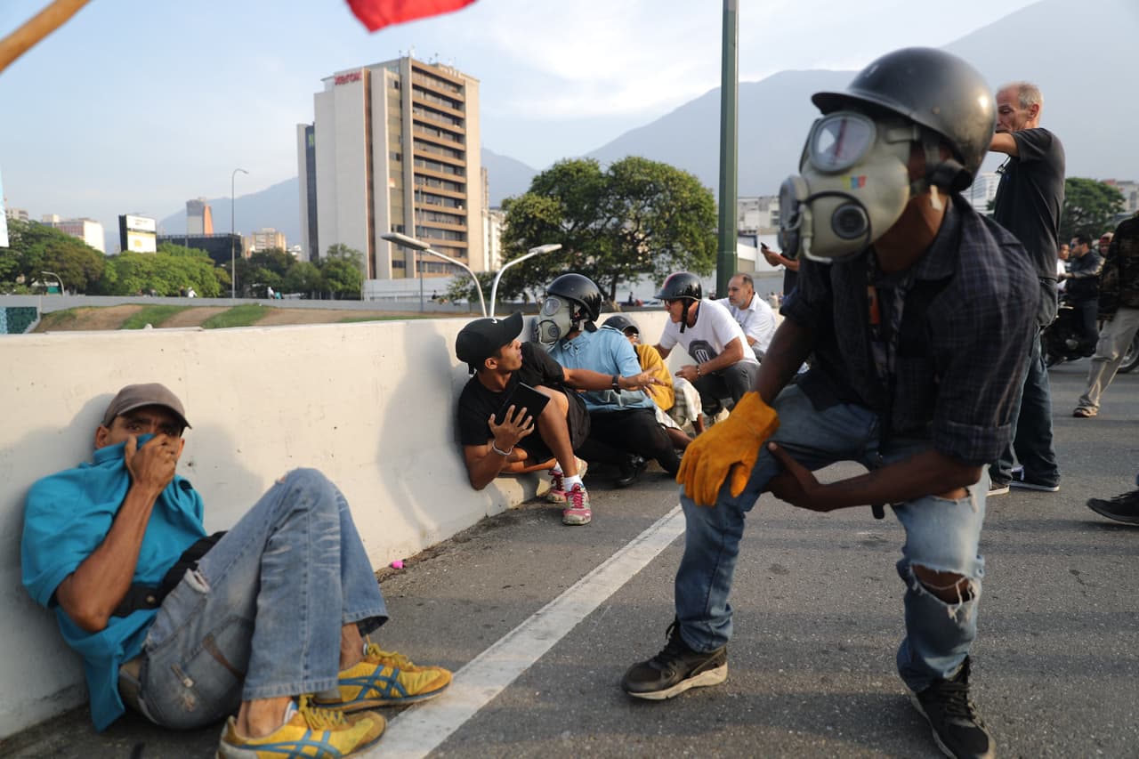 Simpatizantes de Juan Guaidó se protegen de las bombas lacrimógenas que arrojan las fuerzas de seguridad leales a Maduro.