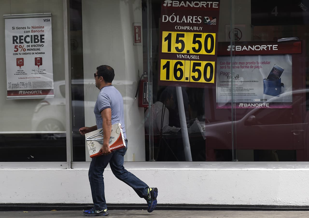Un hombre camina frente a un banco en Ciudad de México el 30 de julio de 2015: el mismo día que el Banco Central mexicano anunció que aumentaría las subastas diarias, de 52 millones a 200 millones de dólares sin mínimo de depreciación, para apuntalar el valor del peso. Ese año, la moneda había perdido casi el 20% de su valor frente al dólar. (María Calls / AFP)