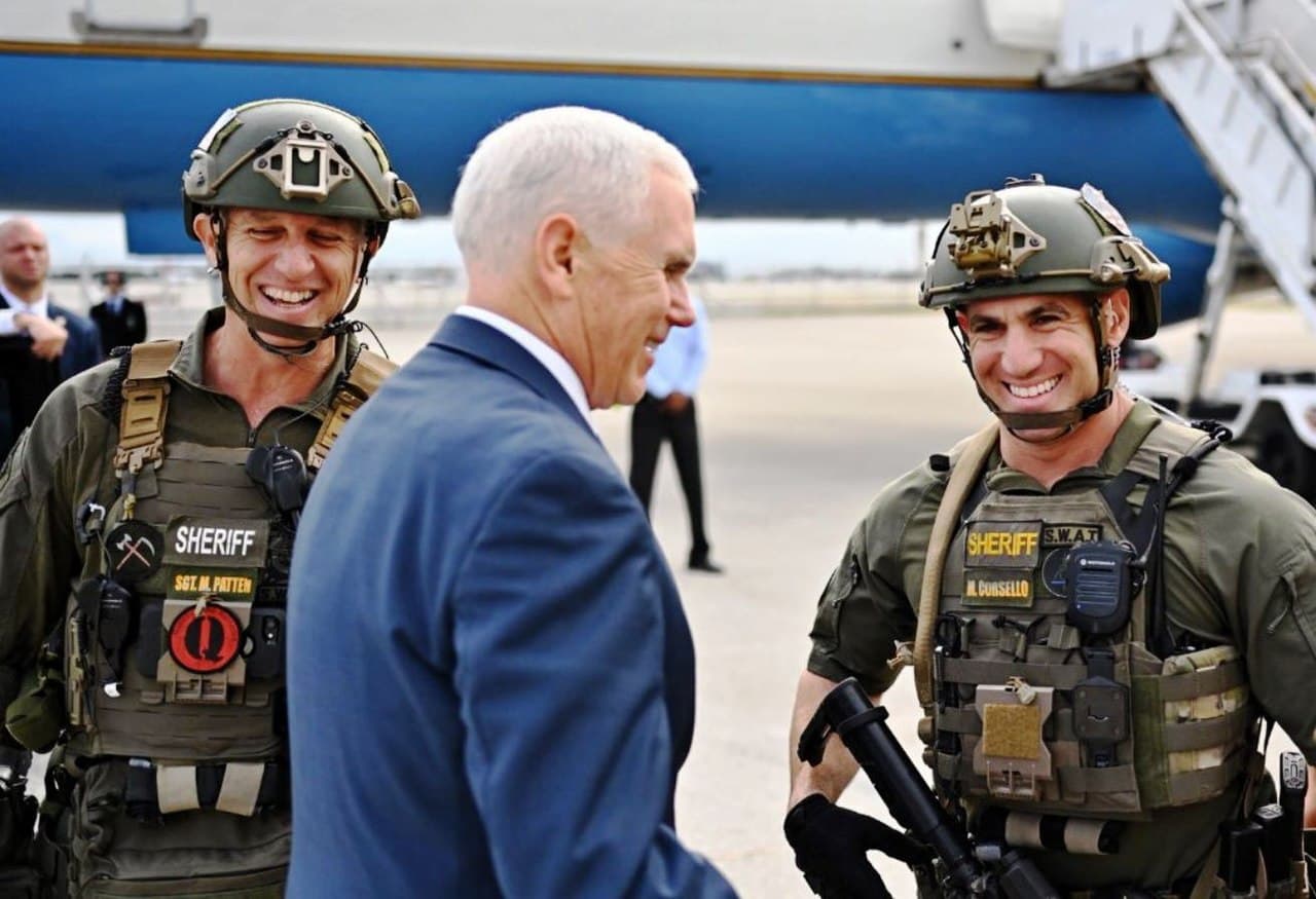 Un integrante (izq.) del equipo SWAT del Condado de Broward en Florida, fue sancionado por recibir al vicepresidente Mike Pence, con el símbolo de QAnon en su uniforme en noviembre de 2018.