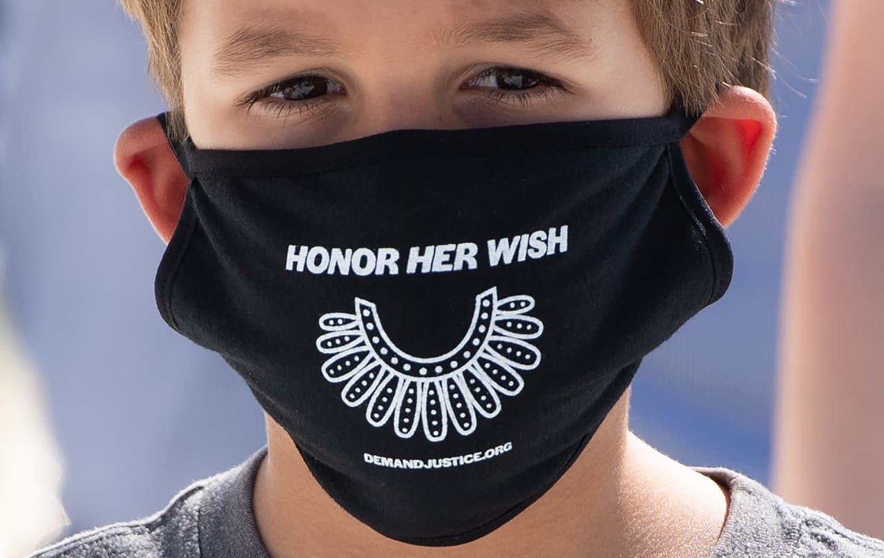 Un niño llevó al Máximo Tribunal una mascarilla con la frase "honremos su deseo", en referencia al anhelo de Ginsburg de que su reemplazo sea hecho después de las elecciones de noviembre. En la tela también está impresa una referencia al icónico collar.