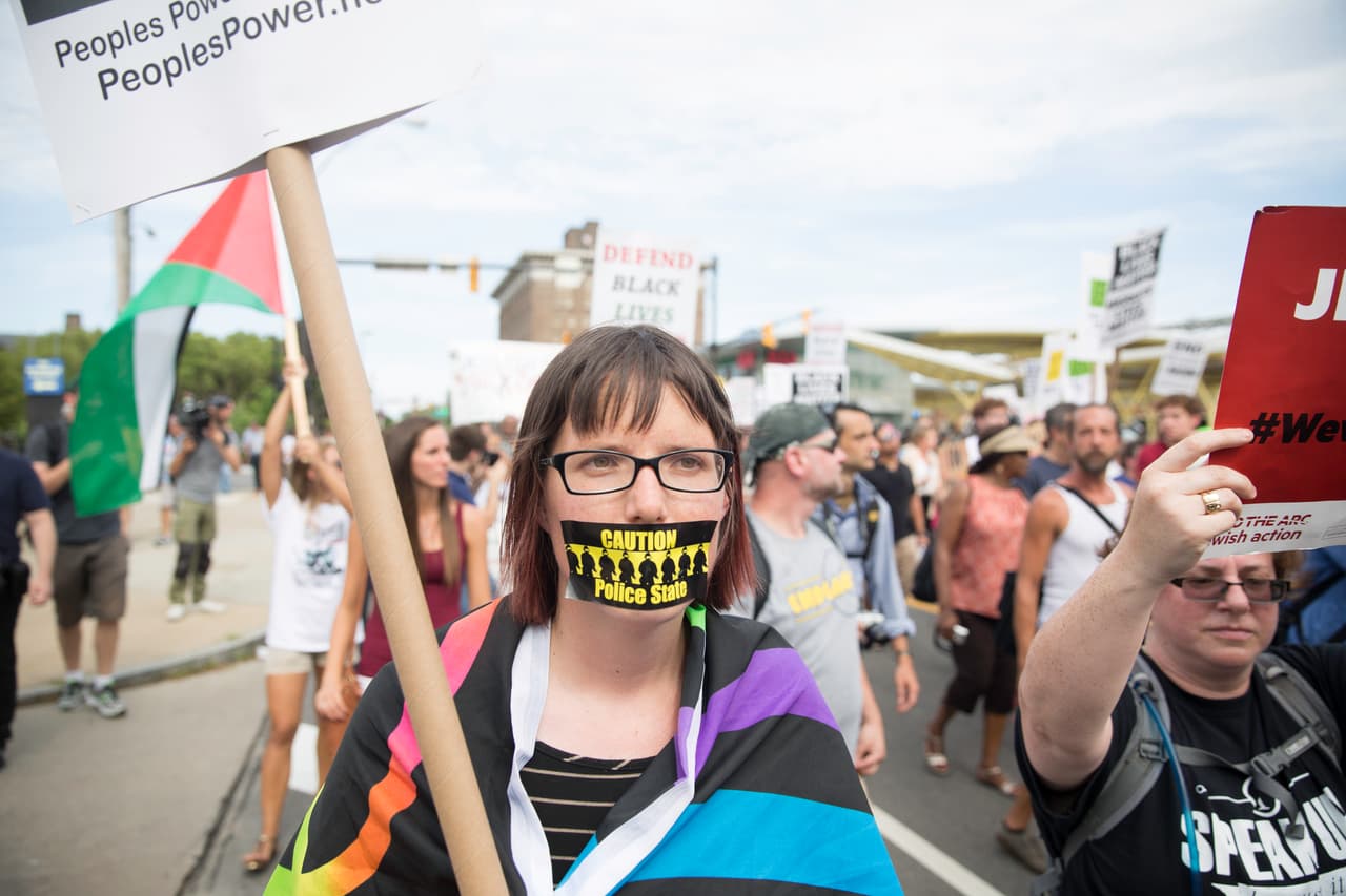 “Precaución, estado policial” se lee en el cartel que tapa la boca de esta manifestante.