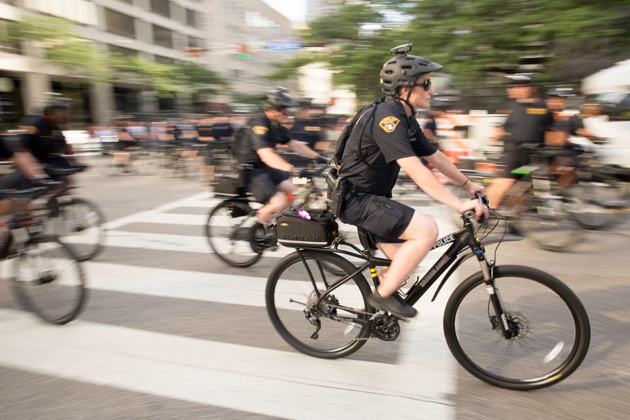 DOMINGO 17 DE JULIO. 6:30 PM. Los policías ciclistas se mueven rápido. El centro de Cleveland no tiene grandes subidas o bajadas y los oficiales, algunos listos con equipos antimotines y cámaras en sus cascos, parecen adelantarse a cualquier acontecimiento. El domingo todavía parece una tarde de fogueo para el organizado grupo.