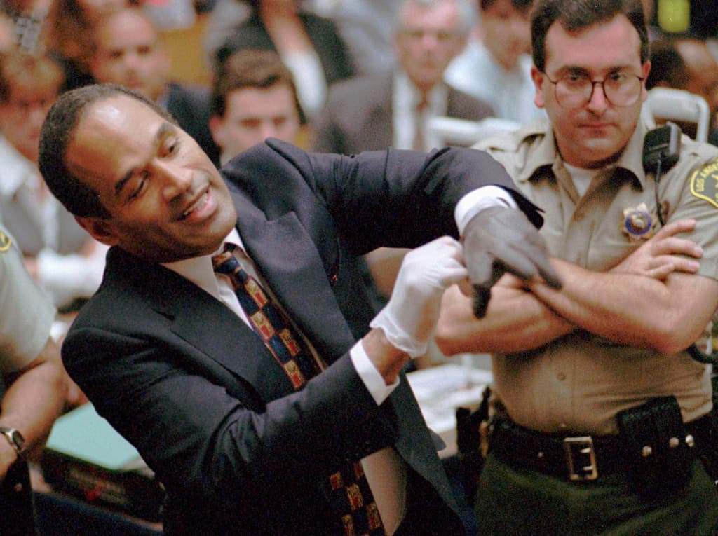 En esta fotografía de archivo del 15 de junio de 1995, O.J. Simpson, a la izquierda, hace una mueca mientras se prueba uno de los guantes de cuero que los fiscales dicen que usó la noche en que su ex esposa Nicole Brown Simpson y Ron Goldman fueron asesinados en un tribunal de Los Ángeles.