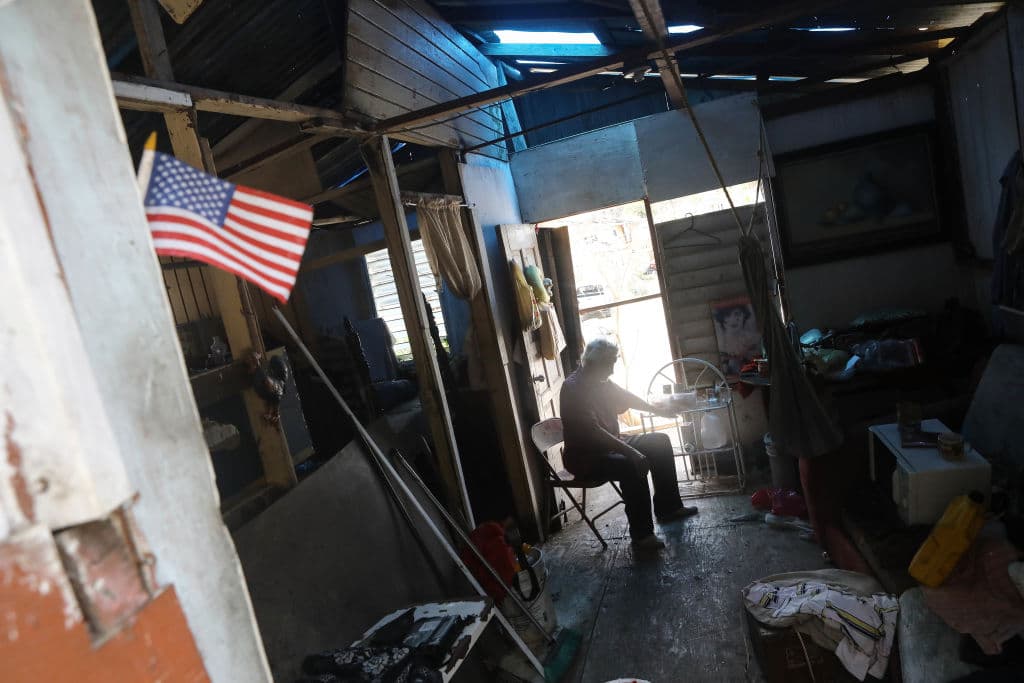SAN ISIDRO, PUERTO RICO - OCTOBER 05: Resident Errol sits in his damaged home without power or running water, decorated with a small American flag, about two weeks after Hurricane Maria swept through the island on October 5, 2017 in San Isidro, Puerto Rico. Puerto Rico experienced widespread damage including most of the electrical, gas and water grid as well as agriculture after Hurricane Maria, a category 4 hurricane, swept through. (Photo by Mario Tama/Getty Images)