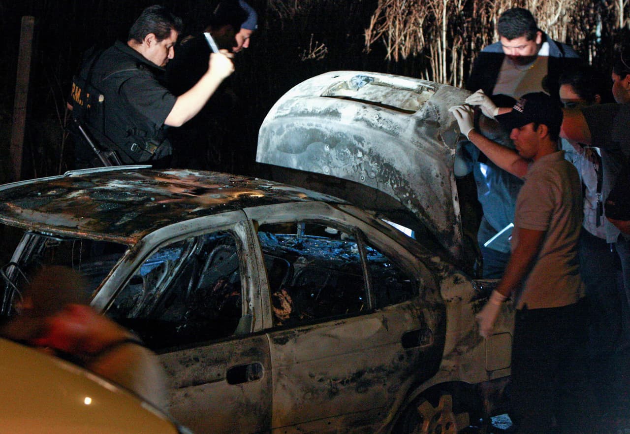 Detectives revisan un vehículo quemado con seis cadáveres en su interior.