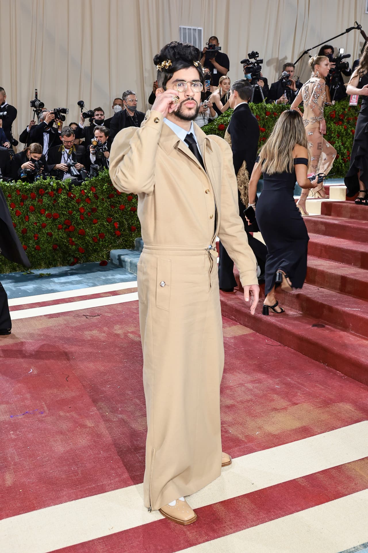 <b>Bad Bunny</b> dejó ver que no le pone etiquetas de género a la moda con un look de una gabardina con una falda larga de la casa Burberry. Para su peinado llevó un par de caireles a lado y un moño alto.
