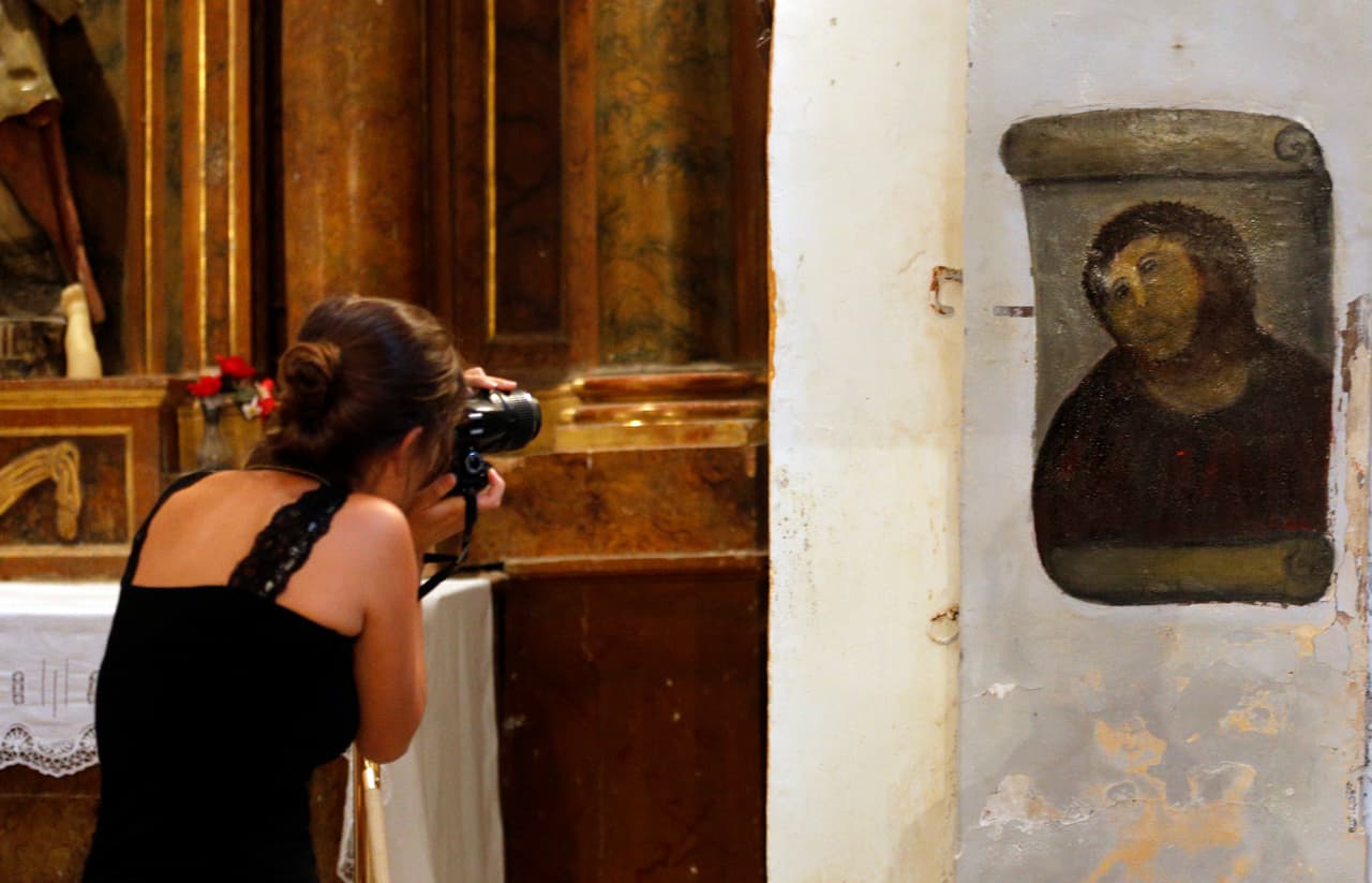 Una mujer toma fotografías de la versión ‘restaurada’ de la obra ‘Ecce Homo’, hecha originalmente por el pintor Elías García Martínez en 1910. Iglesia Borja de Zaragoza, 28 de agosto de 2012.