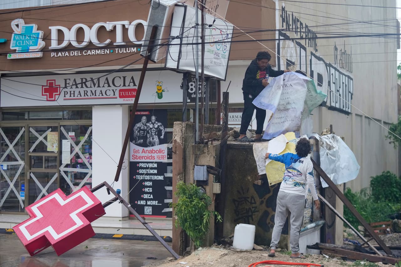 Vecinos limpian la entrada de una farmacia dañada por el huracán Beryl.
