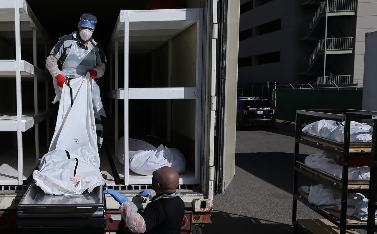 Un recluso ayuda a un funcionario a mover un cuerpo envuelto en bolsa plástica hacia el tráiler de refrigeración temporal que se encuentra en el estacionamiento de la Oficina de Medicina Forense en El Paso, Texas.