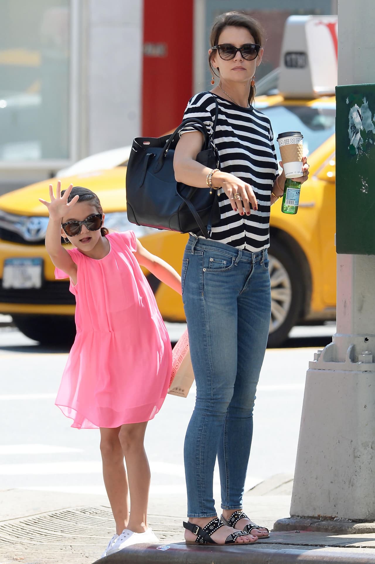 Katie y Suri esperando un taxi en la calle de Los Ángeles. A Suri se le ve el desparpajo de su padre.