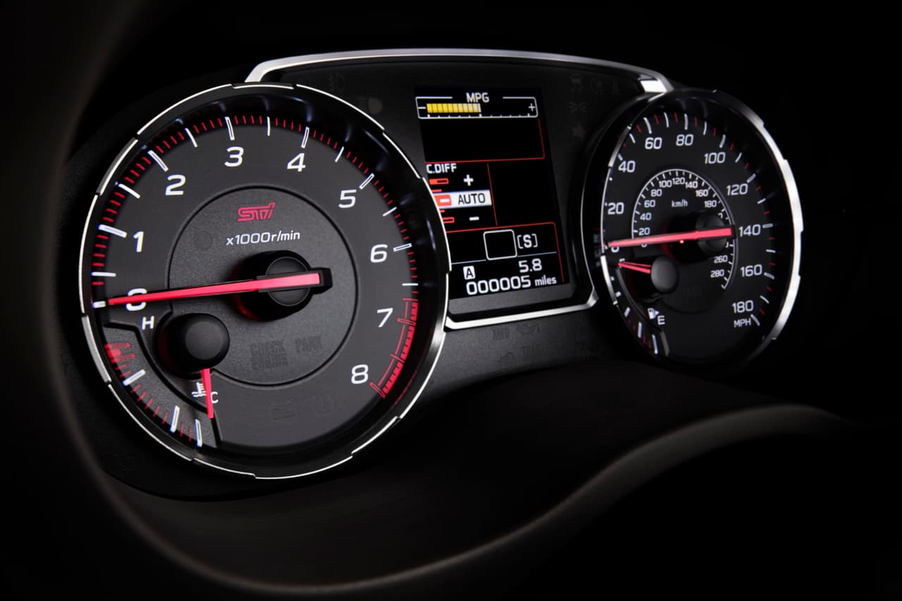 Su tablero muestra tacómetro y velocímetros convencionales, con indicación hasta 180 millas por hora, y una pequeña pantalla central. Las agujas son rojas sobre fondo negro con diales blancos.