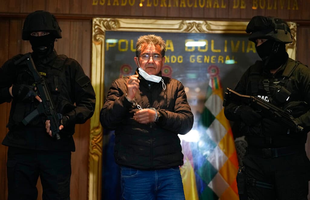 Policías escoltan al excoronel de la policía Maximiliano Dávila (centro) durante su presentación ante los medios de comunicación en la oficina del Comando General de la Policía Boliviana, en La Paz, el domingo 23 de enero de 2022. (AP Foto/Juan Karita)