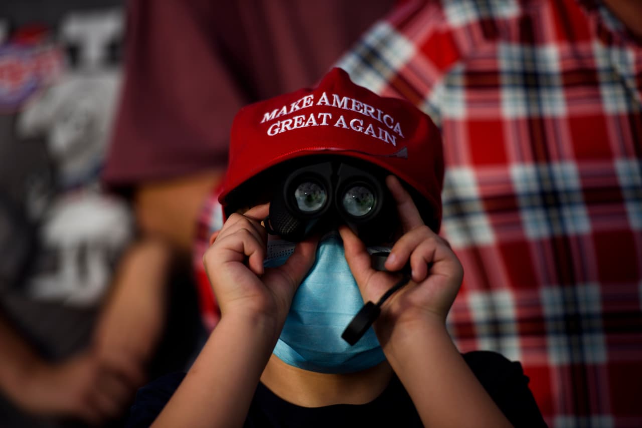 Vistiendo una gorra de 'Make America Great Again', un niño es visto usando binoculares para ver de cerca a Donald Trump.