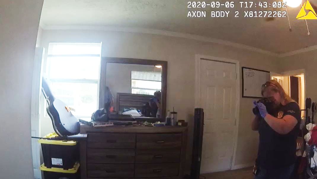 Un agente de policía tomando fotos de la habitación de Alex Bello-Ortiz el día del incidente. Se puede ver un rifle sobre unos contenedores de plástico, abajo a la izquierda.
<br>