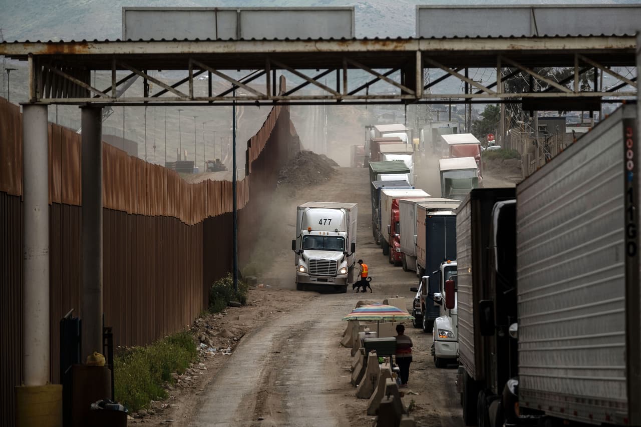 Los camiones que trasladan mercancías a través de la frontera entre México y EEUU han quedado varados hasta más de doce horas tras la aplicación de una nueva medida del gobierno estadounidense de reubicar agentes para agilizar los trámites migratorios acumulados. En la fotografía decenas de transportistas esperan junto a la valla fronteriza cerca de la aduana entre Tijuana y San Isidro, el jueves 4 de abril.