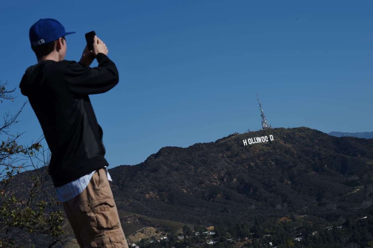 Tourists visiting the Hollywood Bowl Overlook see the Hollywood sign reading "Hollywoed" before repair crews completed their work to return the sign to its normal state, after vandals converted it to read "Hollyweed," January 1, 2017 in Hollywood, California. Police said unidentified thrill-seekers had climbed up and arranged tarps over the two letter "O's" to make them look like "E's," CBS affiliate KCAL reported. Each letter is 45 feet (13.7 meters) high, so the feat would have required not just bravado but considerable athleticism. / AFP / Robyn Beck (Photo credit should read ROBYN BECK/AFP/Getty Images)