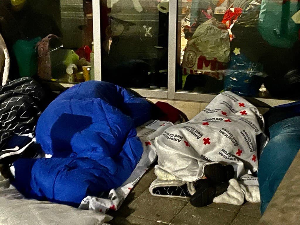 Migrantes en las calles envueltos en sacos para dormir y protegerse del frío.