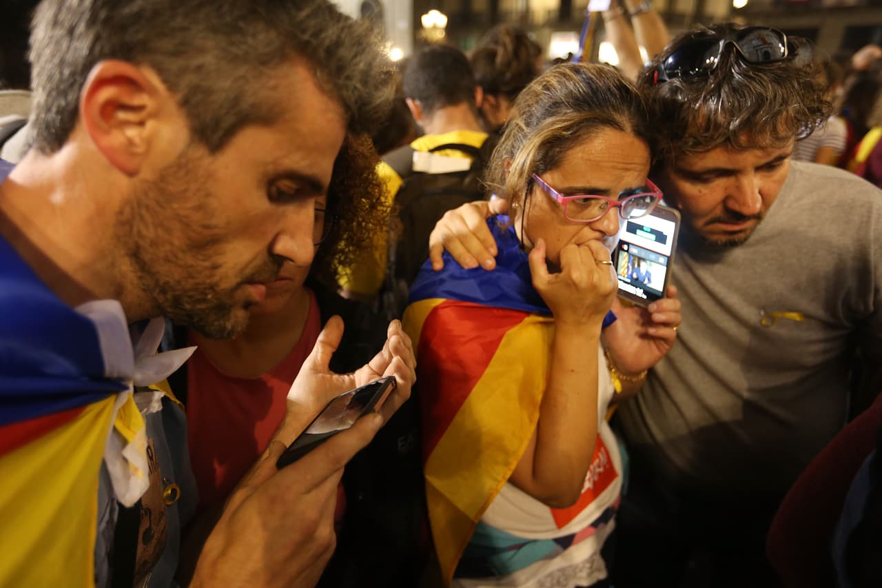 Un grupo de personas escucha en sus celulares el discurso del presidente de Cataluña, Carles Puigdemont, la noche del sábado mientras protestaban frente al Palacio de la Generalitat, que alberga la sede del Ejecutivo en Barcelona. (Sean Gallup/Getty Images)