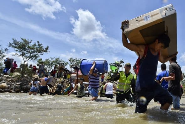 Colombianos deportados por Venezuela cruzan sus pertenencias a través del río Táchira..