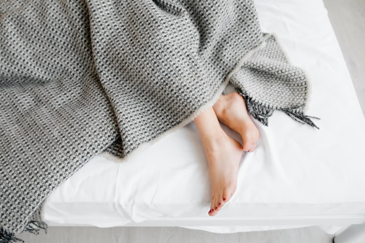 Female feet under blanket flat lay. Female beautiful feet with red pedicure on the bed. Top view on the sleeping woman legs under gray blanket