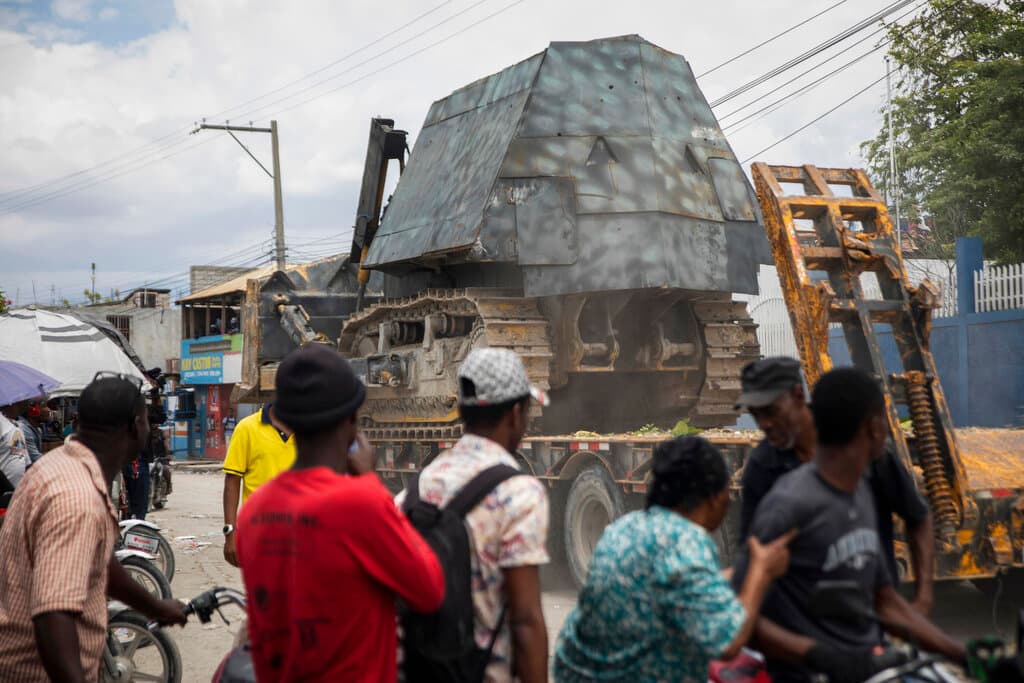 Los residentes observan cómo un coche de policía blindado es transportado en la plataforma de un remolque, para ser utilizado en una operación antipandillas en Croix-des-Missions, al norte de Puerto Príncipe, Haití, el jueves 28 de abril de 2022.