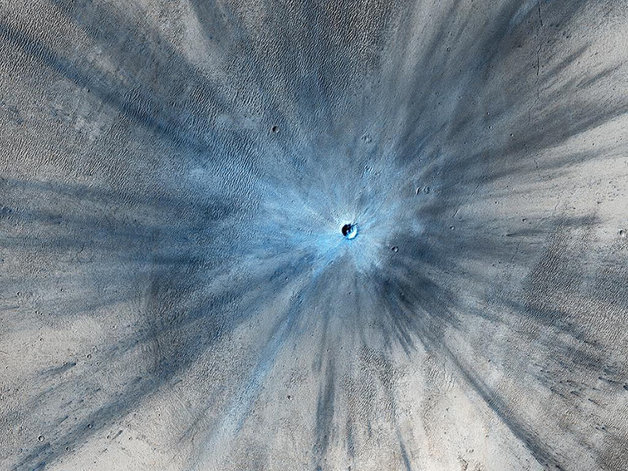 Esta imagen del cráter que dejó el impacto reciente de un meteorito fue tomada por la cámara HiRISE del orbitador Reconnaissance, en noviembre de 2013. El cráter está rodeado por una gran zona que muestra la violencia del impacto.