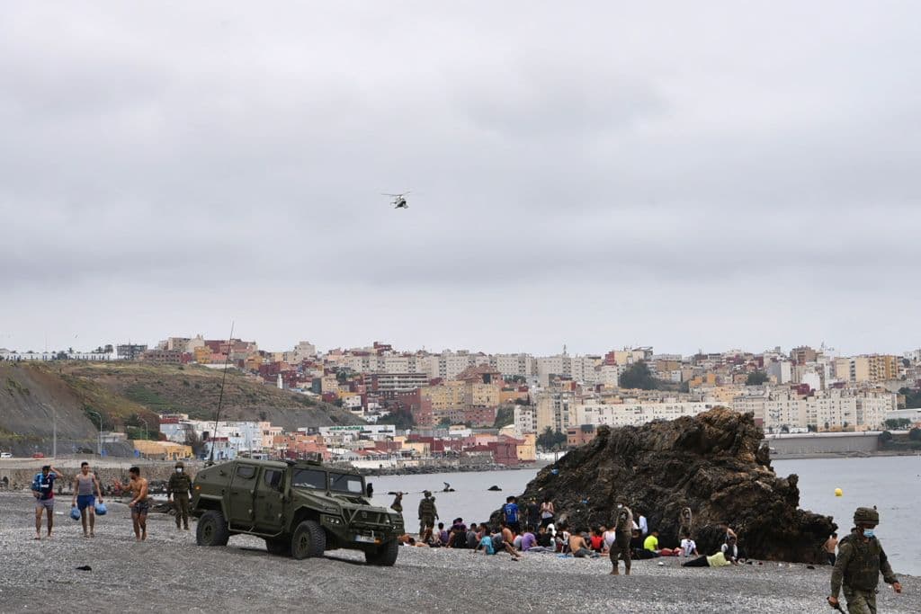 En la imagen se observa a los migrantes que llegaron nadando a Ceuta. En la playa descansan mientras los soldados españoles hacen guardia. Para tratar de controlar la situación, el Gobierno de España ha desplegado este martes 
<b>varias unidades del Ejército de Tierra a las naves del Tarajal</b>, donde se concentra a buena parte de los inmigrantes, especialmente los menores de edad.