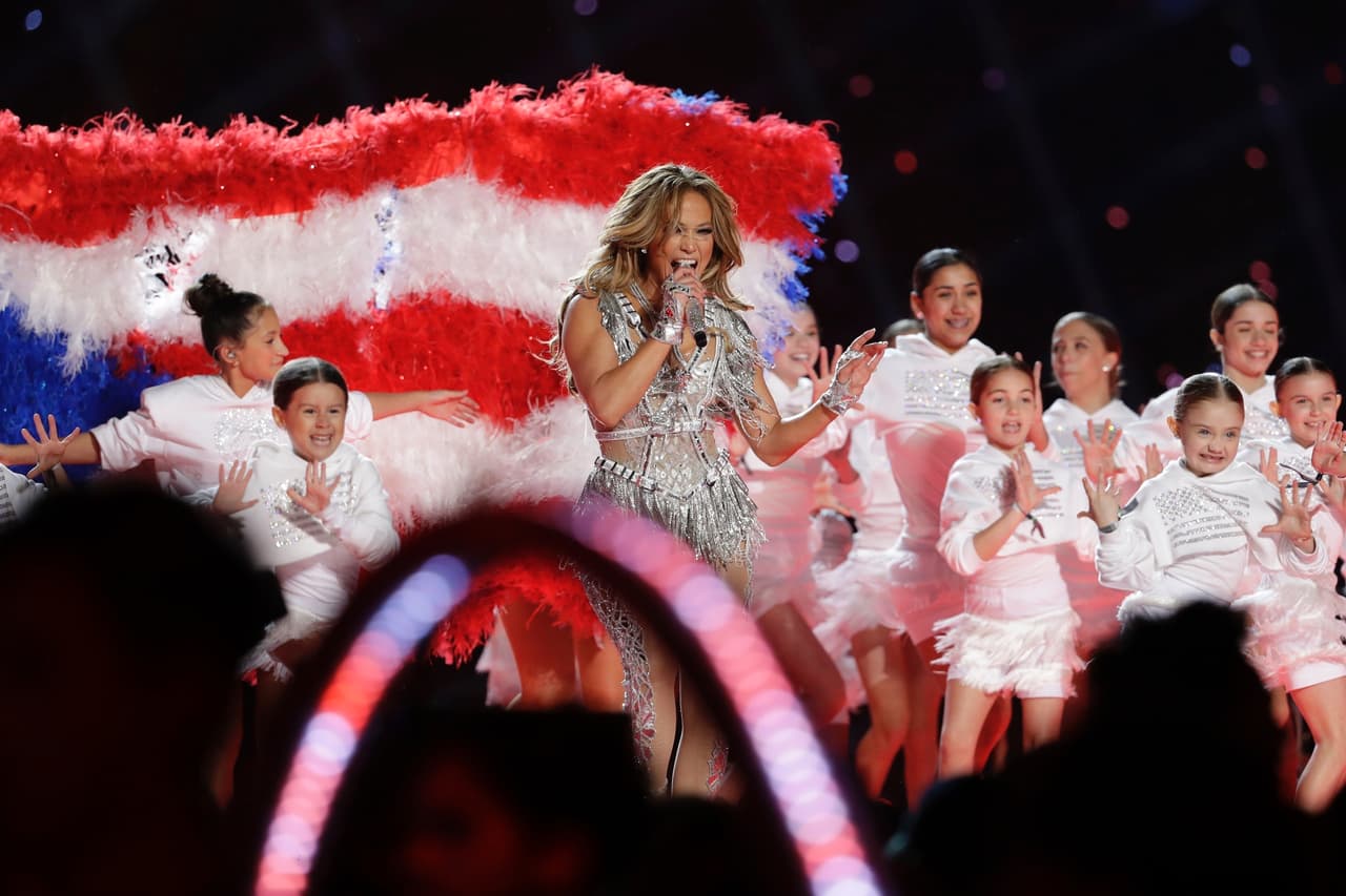 Jennifer Lopez cantando con un coro de niños y con una bandera de Puerto Rico al fondo.
