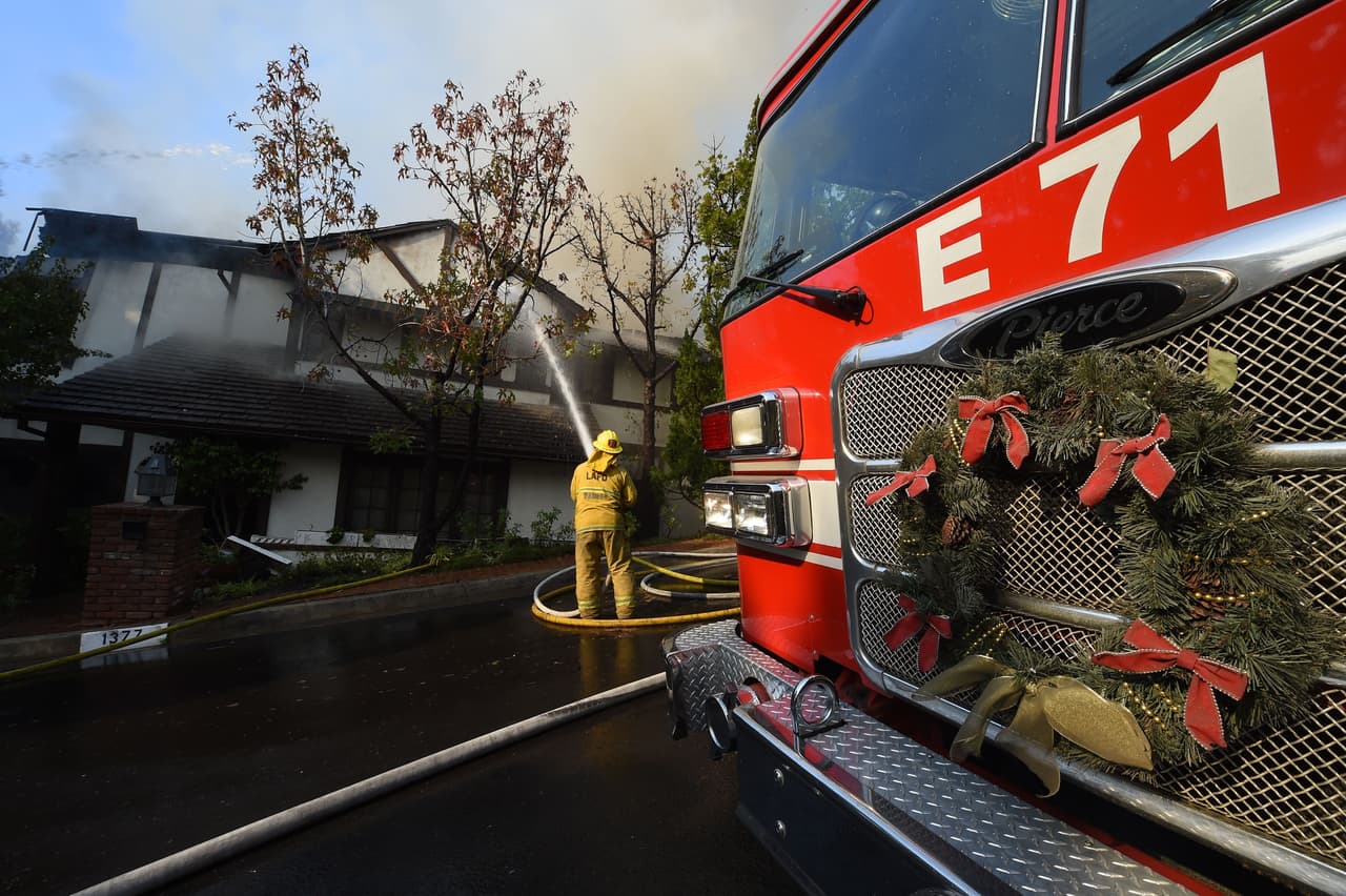 Un bombero riega preventivamente una casa a punto de incendiarse en Bel-Air. El camión de los Bomberos de Los Ángeles lleva un aro navideño.
