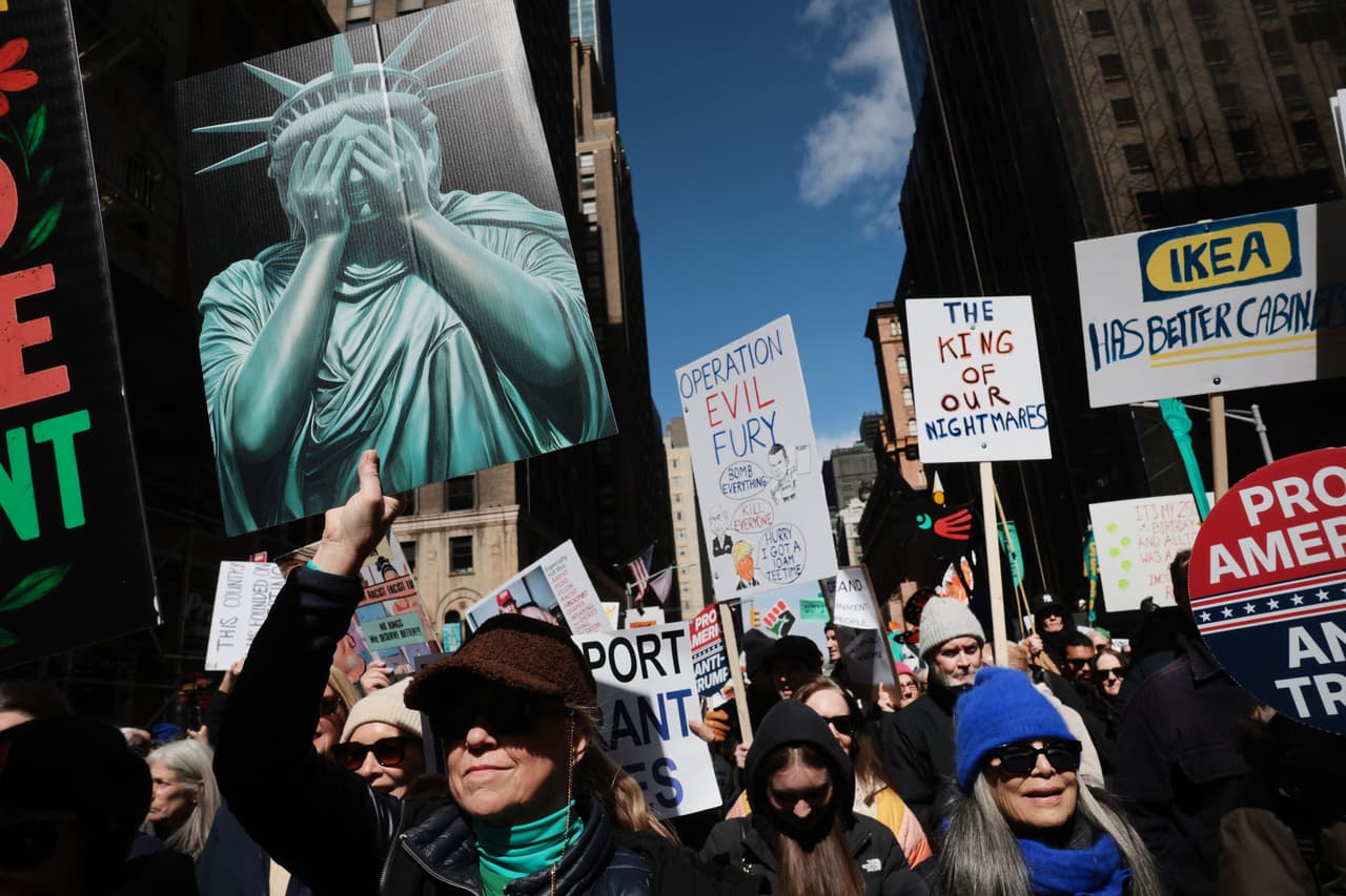 La Estatua de la Libertad se 'tapa' el rostro ante la situación política y social en Estados Unidos, donde manifestantes levantan pancartas mientras participan en la protesta “No Kings” en Manhattan, Nueva York.