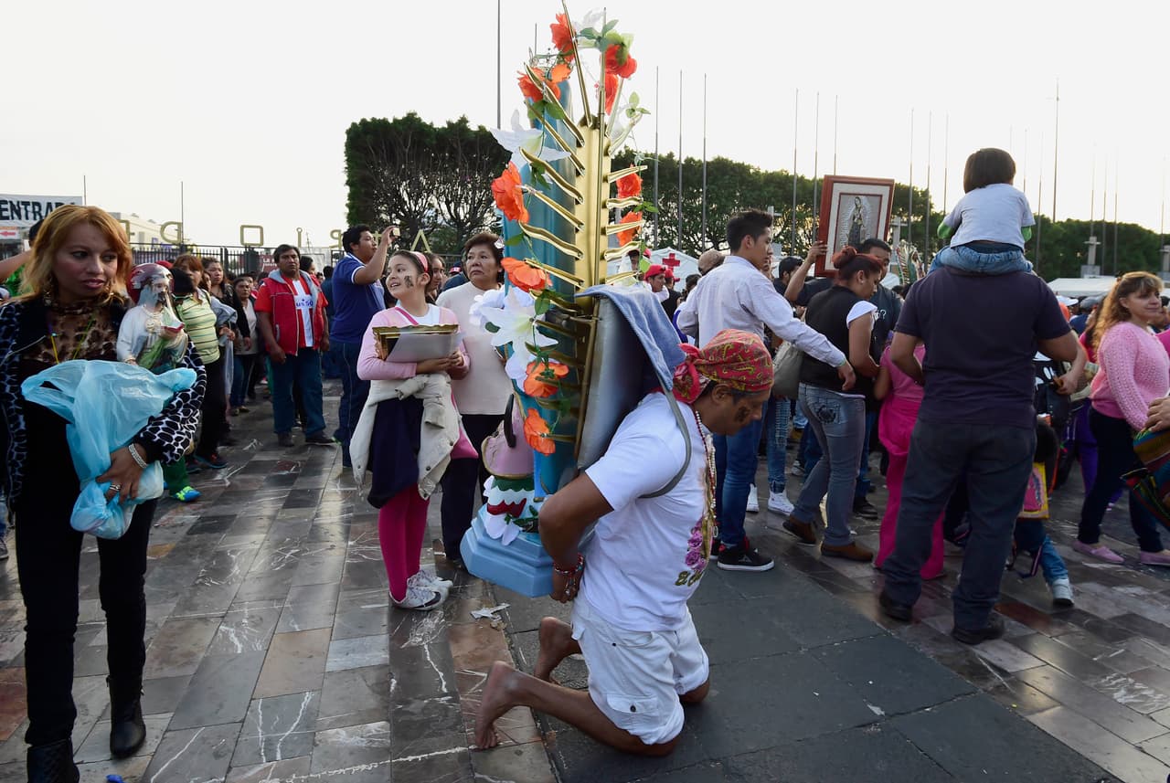 Un hombre carga una enorme imagen de la Virgen de Guadalupe sobre su espalda.