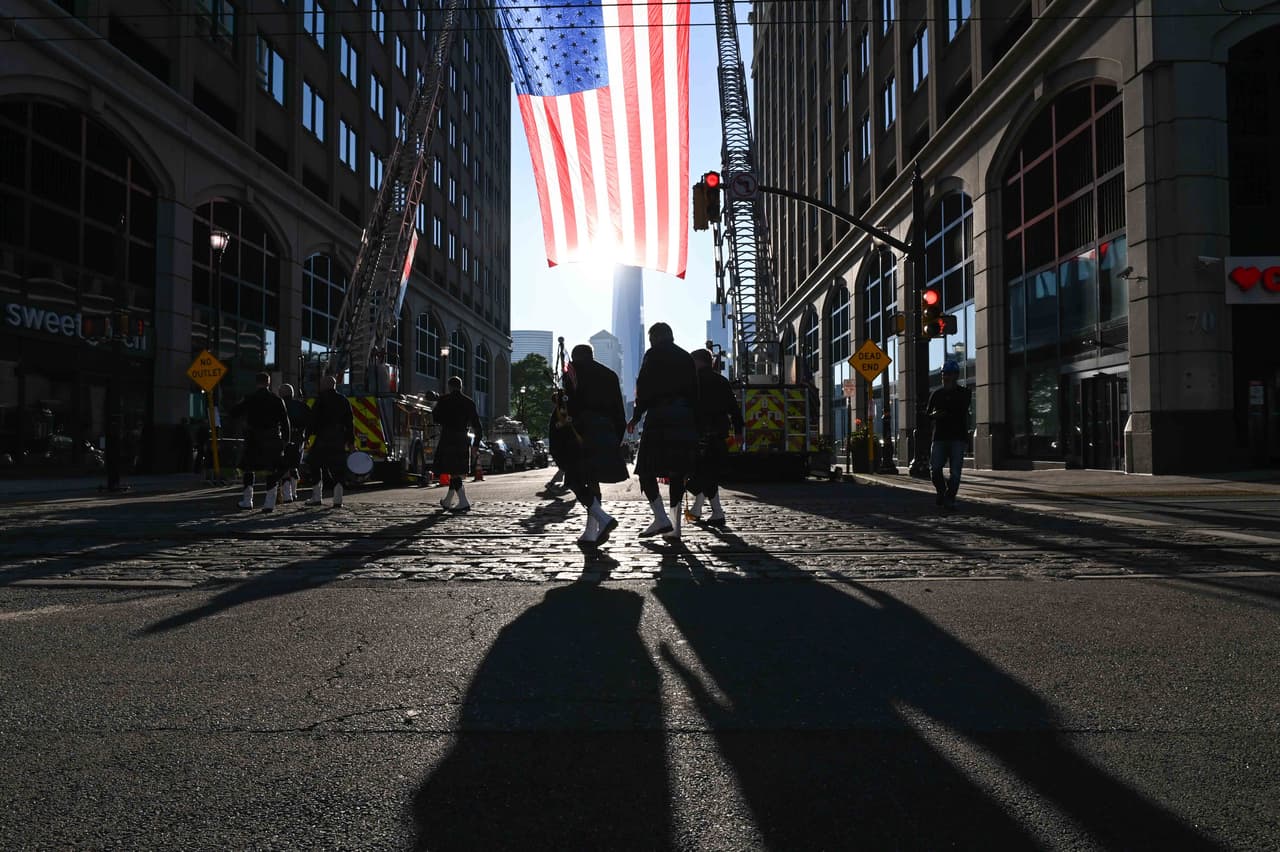 Miembros de la banda New Jersey Piper pasan debajo de una inmensa bandera en Jersey City, al frente de Nueva York, a la otra orilla del río Hudson.