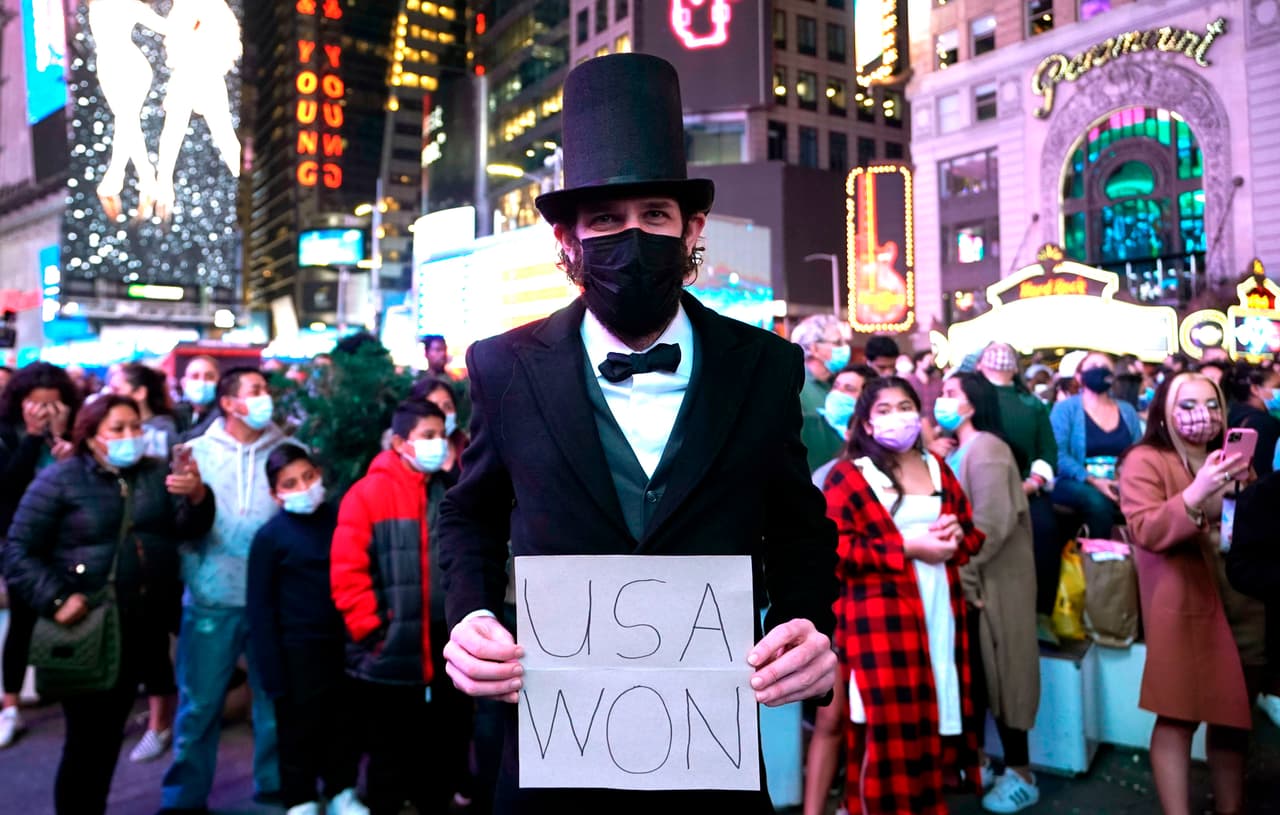 Un hombre vestido como Abraham Lincoln sostiene un cartel mientras la gente celebra en las calles de Times Square, antes de que el presidente electo de EE. UU. Joe Biden pronuncie un discurso desde Delaware.
