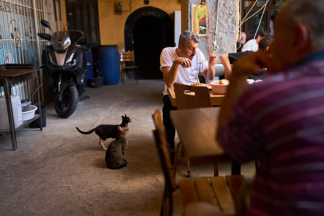 Artesanos almuerzan mientras los gatos merodean cerca durante un descanso en el barrio artesanal de Buyukhan en Estambul.