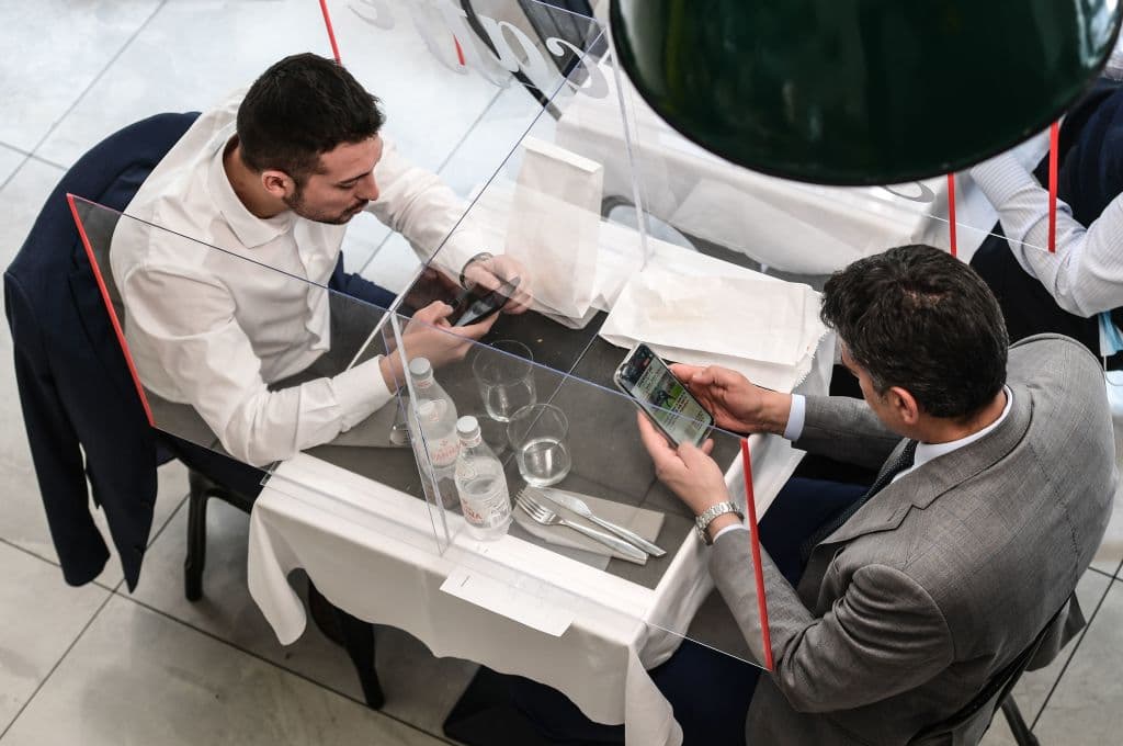 Personas almorzando en una mesa dividida con plexiglás en el Café Goga el 18 de mayo de 2020 en el centro de Milán. Además de las iglesias, los restaurantes reabrieron en Italia, el último paso del país en un regreso prudente y gradual a la normalidad.