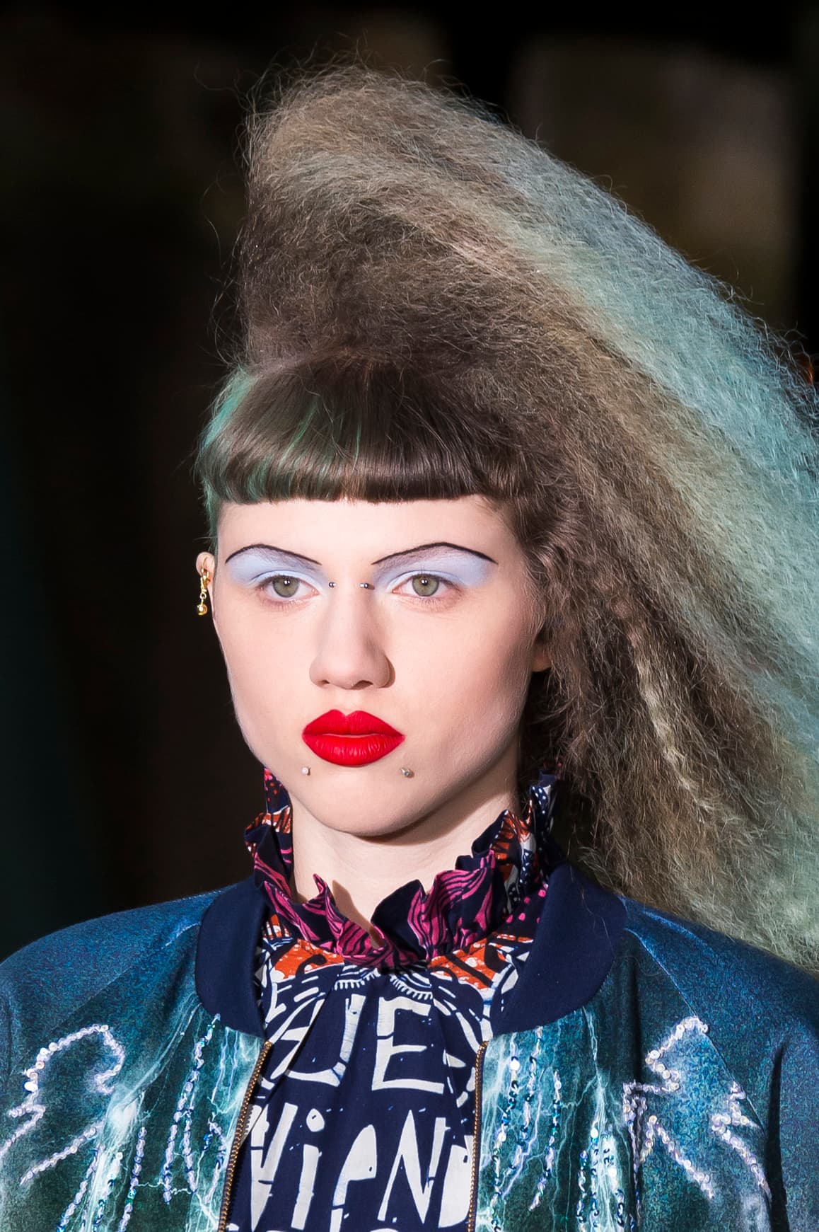 Para nostálgicos ochenteros, esta propuesta de 
<a href="http://www.vogue.com/fashion-shows/fall-2016-ready-to-wear/manish-arora/slideshow/collection#16">Manish Arora</a>. El peinado se consigue con una wafflera. Si no tienes una, trenza en pequeñas secciones el pelo húmedo y deja que seque, luego desházlas y esponja el pelo con una secadora. Unas sombras azul claro y unos labios rojos en acabado mate son básicos para lograr el 
<i>look</i>. El trazo definido de las cejas es clave para darle el toque de disfraz.
<br>