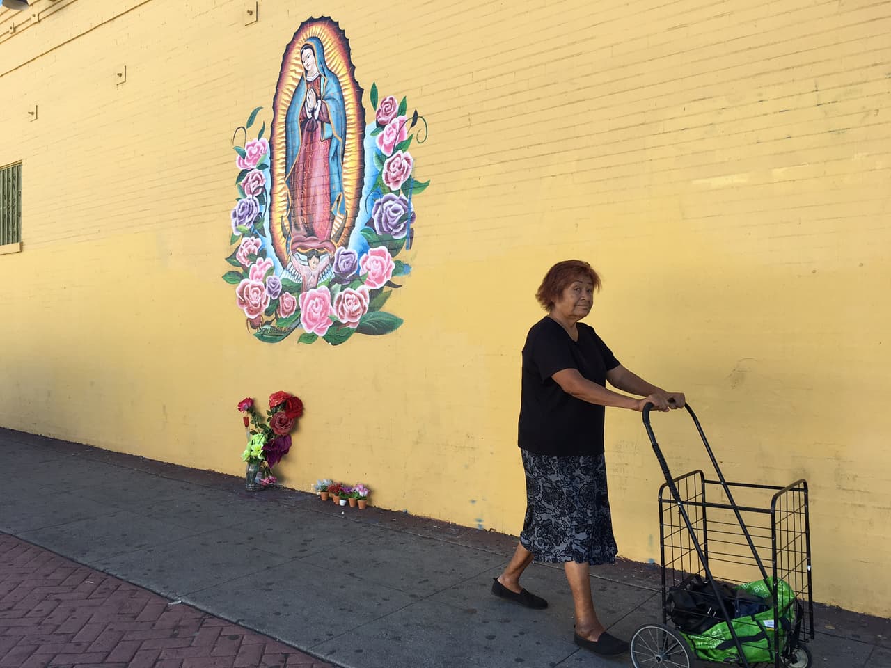 Una mujer camina frente a una imagen de la Virgen en la pared de una lavandería de Los Ángeles que han respetada las pintas de los pandilleros.