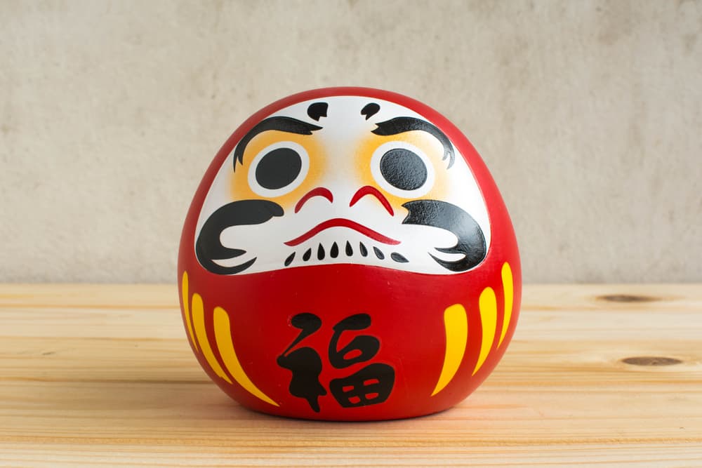 <b>Daruma</b>
<br>Este muñeco rojo representa al monje Bodhidharma, fundador del budismo Zen, quien habría perdido las manos y pies al estar meditando por un largo tiempo, por lo que carece de brazos y piernas. Cuenta con un bajo centro de gravedad que le permite recuperar su postura original si llega a caer, simbolizando con ello la perseverancia y el optimismo.